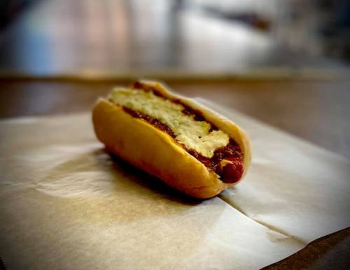 A hot dog in a bun topped with chili and cheese, resting on a piece of parchment paper.