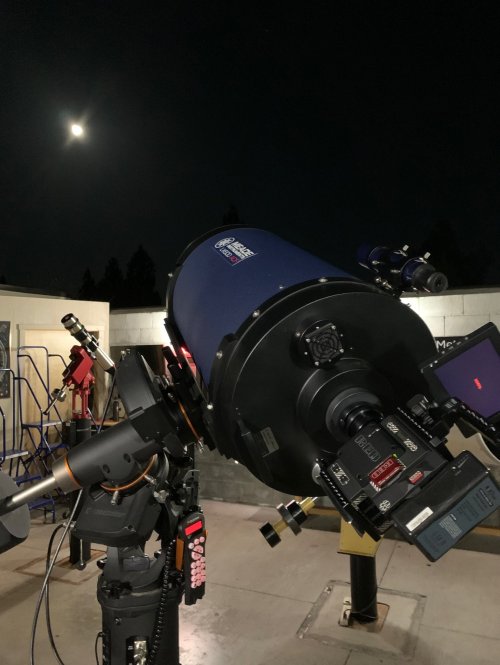 A telescope pointed at the night sky, with the moon visible in the background.