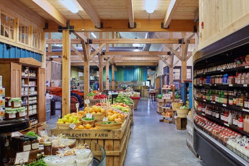 A bright, spacious market interior with wooden beams, showcasing fresh produce and various local products on display.