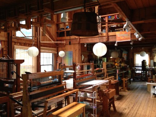 A cozy workshop filled with weaving looms, wooden furniture, and soft lighting from hanging lanterns.