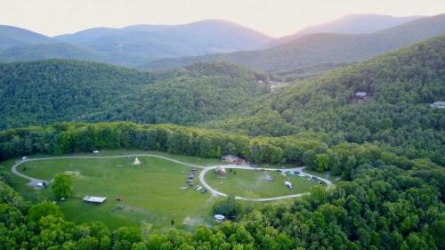 Aerial view of a lush green valley surrounded by mountains, featuring a circular field and scattered tents.