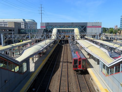 A train station with platforms, tracks, and a modern building under a clear blue sky.