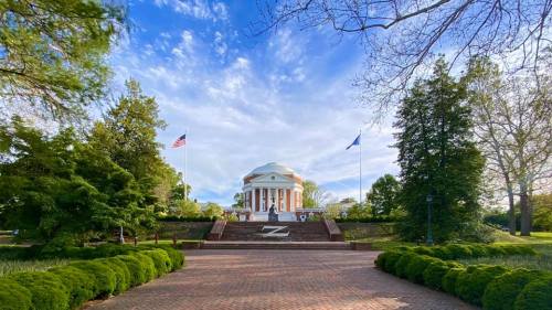 A scenic view of a circular building surrounded by trees, flags, and a brick pathway under a blue sky.
