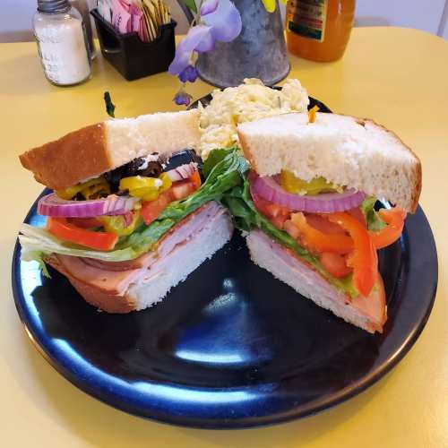 A sandwich with layers of lettuce, tomato, onion, and ham, served on a black plate with a side of scrambled eggs.