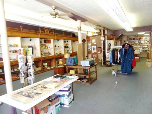 A vintage shop interior with wooden shelves, various items for sale, and a mannequin dressed in a coat.