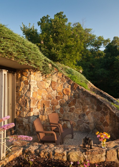A cozy outdoor seating area with stone walls, lush greenery, and colorful flowers in the foreground.