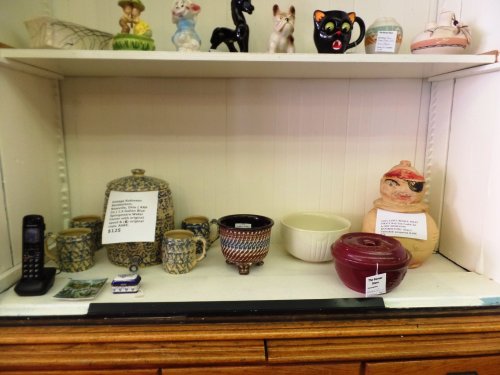 A display shelf with various vintage items, including pottery, a phone, and decorative figurines. Price tags visible.