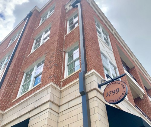A brick building with large windows and a sign reading "1799 Kitchen and Cocktails" hanging from the side.