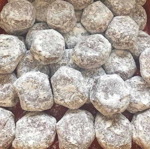 A close-up of hexagonal pastries dusted with powdered sugar, arranged in a red container.