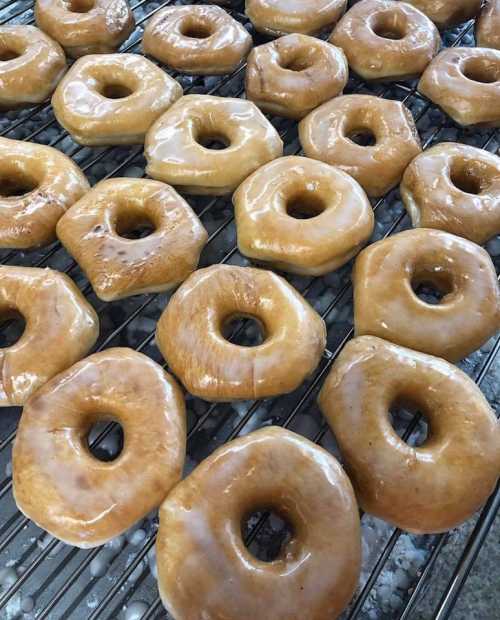 A close-up of freshly glazed donuts cooling on a wire rack, showcasing their shiny, golden-brown surface.