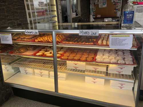 A display case filled with various donuts, labeled "Glazed" and "Mixed," with a hand sanitizer station nearby.