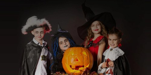 Four children in Halloween costumes pose with a carved pumpkin, featuring a witch, vampire, and other spooky characters.