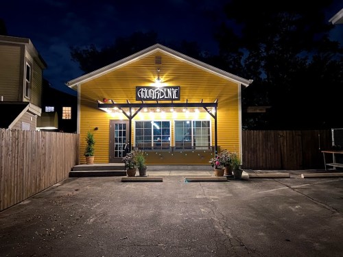 A brightly lit yellow building at night with a sign reading "Cuarentena" and potted plants in front.