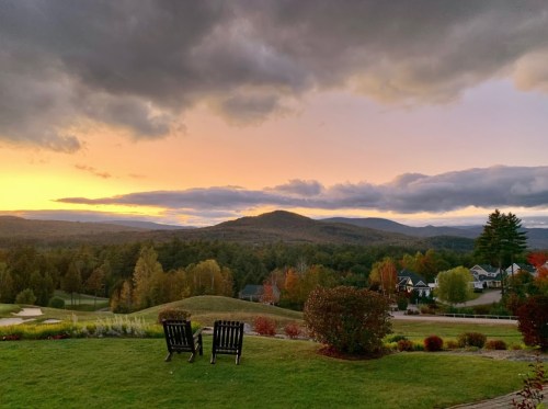 A serene landscape at sunset, featuring two chairs overlooking rolling hills and colorful autumn trees.