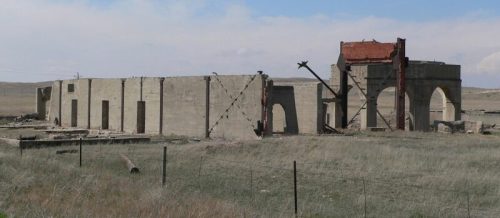 Abandoned concrete building ruins in a grassy landscape under a blue sky.
