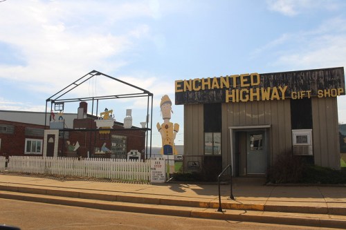 A quirky gift shop with a sign reading "Enchanted Highway" and whimsical characters displayed outside.