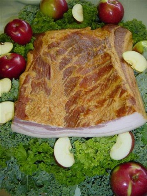 A large piece of cooked meat on a bed of kale, surrounded by red apples and apple slices.