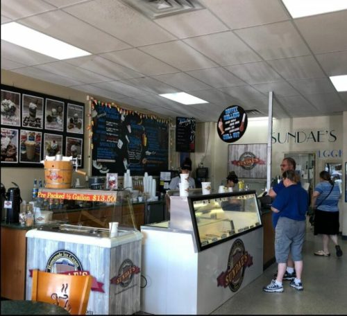 Interior of an ice cream shop with a counter, menu boards, and customers ordering. Bright and inviting atmosphere.