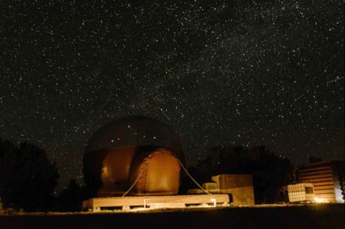 A dark sky filled with stars above a dome-shaped observatory in a remote area.