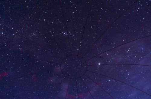 A starry night sky with a circular pattern of lines radiating from the center, creating a web-like effect.