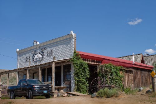 A rustic building with a red roof, wooden porch, and a black truck parked outside under a clear blue sky.