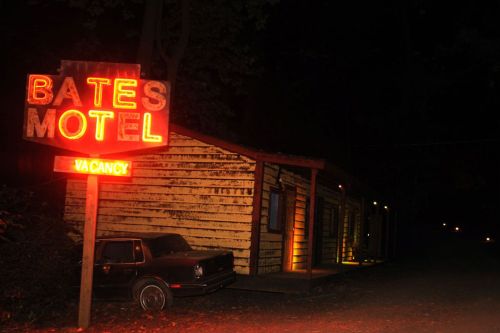 A dimly lit Bates Motel sign at night, with a rustic building and an old car parked nearby.