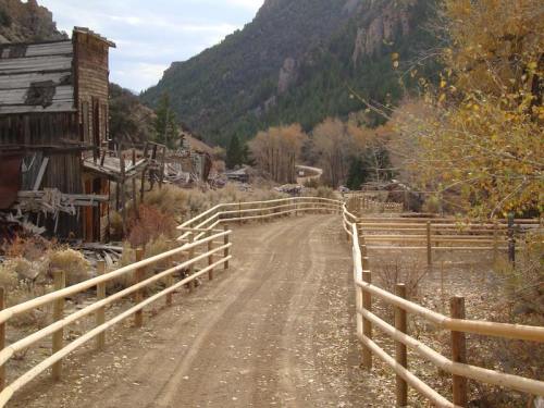 A dirt path winds through a rustic landscape with wooden fences, surrounded by mountains and autumn foliage.