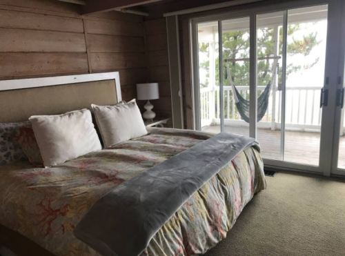 Cozy bedroom with a large bed, decorative pillows, and sliding glass doors leading to a balcony with a hammock.