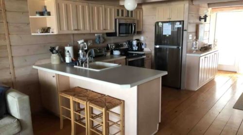 A modern kitchen with light wood paneling, stainless steel appliances, and a central island with bar stools.