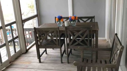 A cozy porch with a wooden table, two chairs, and a bench, adorned with vases of flowers.