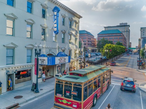 A vibrant street scene featuring a trolley, a historic theater, and modern buildings under a partly cloudy sky.