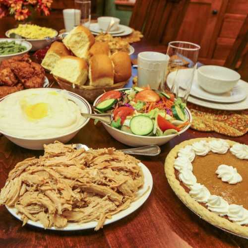 A festive table spread with fried chicken, rolls, mashed potatoes, salad, and pumpkin pie, ready for a celebration.