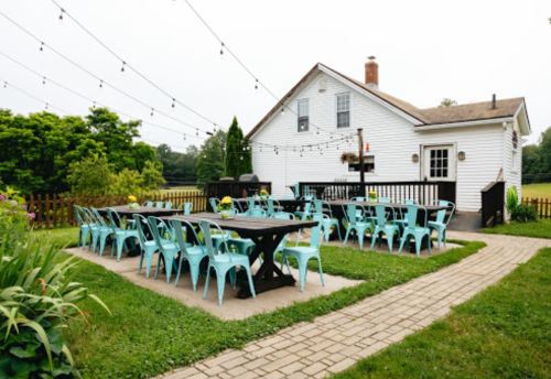 Outdoor dining area with turquoise chairs and tables, string lights, and a white house in the background.