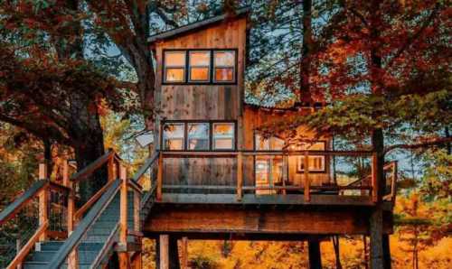 A cozy wooden treehouse elevated among vibrant autumn trees, with warm light glowing from its windows.