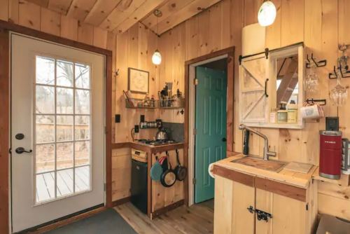 Cozy wooden kitchen with a door to the outside, blue door, and rustic decor, featuring a sink and cooking utensils.