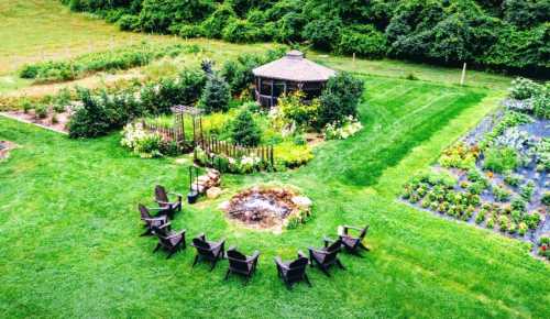 Aerial view of a lush garden with a circular fire pit surrounded by chairs and a gazebo in the background.