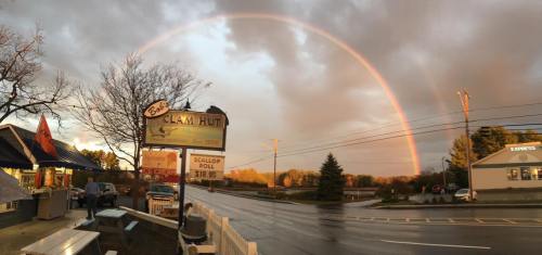 A colorful rainbow arcs over a small roadside eatery, with trees and a cloudy sky in the background.