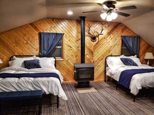 Cozy attic bedroom with two beds, wooden walls, a small stove, and blue accents. Warm and inviting atmosphere.