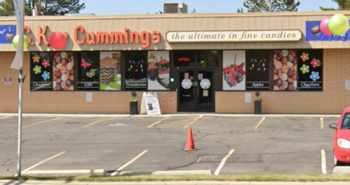 Storefront of C.K. Cummings, featuring colorful candy displays and an "Open" sign, with a red car parked outside.