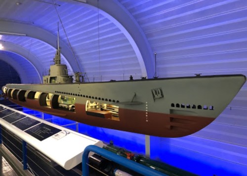 A model of a submarine displayed in a museum, featuring a blue-lit background and detailed interior sections.