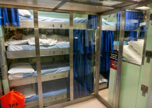 A view of a shared sleeping area with bunk beds, blue curtains, and a fire safety sign visible.