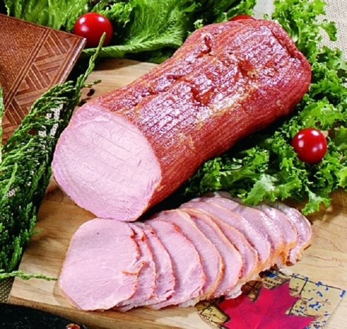 Sliced pink meat on a bed of greens, with whole piece beside it, garnished with cherry tomatoes.