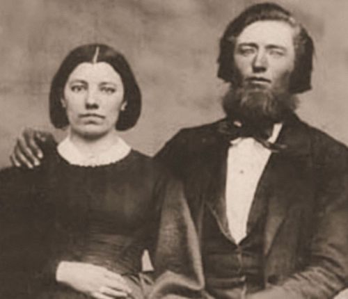 A sepia-toned portrait of a man and woman seated together, both dressed in 19th-century attire, with serious expressions.