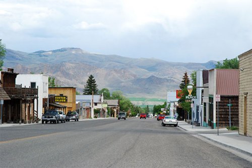 A quiet street in a small town, lined with shops and mountains in the background under a cloudy sky.
