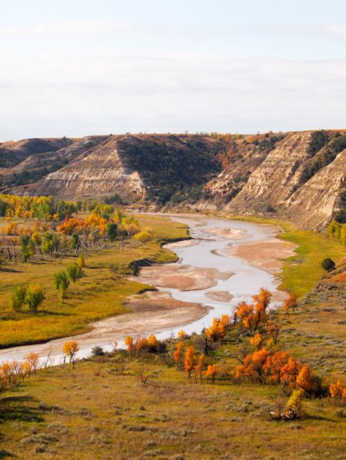 A winding river flows through a valley surrounded by colorful autumn foliage and rugged hills.