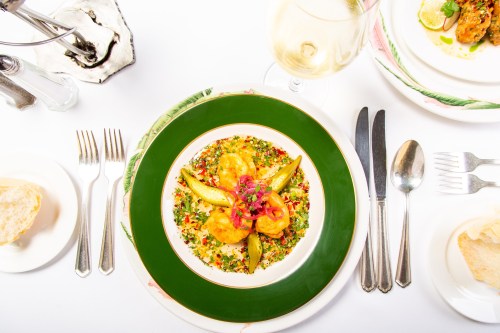 A colorful plate of shrimp and vegetables garnished with herbs, served with a glass of white wine and bread on the side.