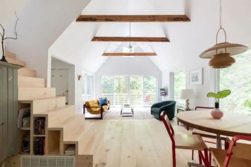 Bright, modern interior with wooden beams, a dining area, and a cozy living space featuring large windows and greenery outside.
