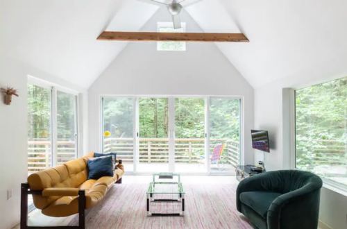 Bright, modern living room with large windows, a yellow sofa, green armchair, and a glass coffee table.