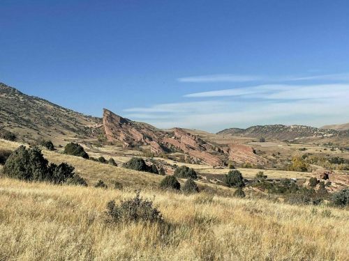 A scenic view of rolling hills and rock formations under a clear blue sky, with grassy fields in the foreground.