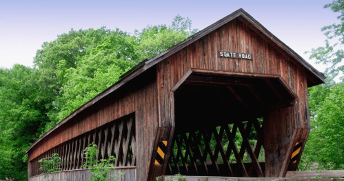 A wooden covered bridge labeled "State Road" surrounded by lush green trees.